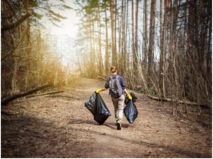 A person carrying 2 large black trash picked up in the woodlands