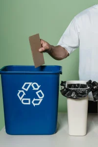 Recycle bin, trash, and arm holding cardboard over recycle bin