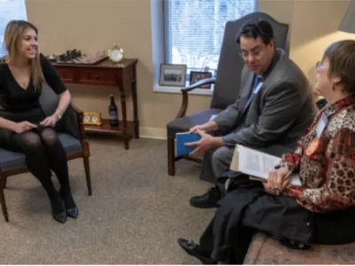 Three people sitting in a room with chairs and couch talking - preparing to meet with public officials